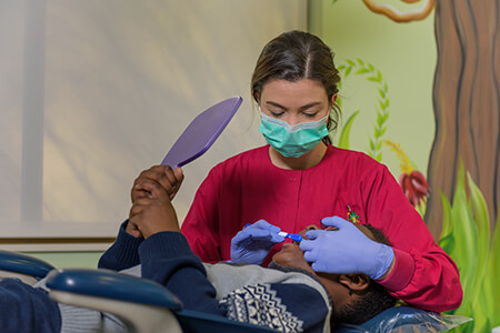 Picture of dental assistant with child going over teeth brushing while child sits in medical recliner
