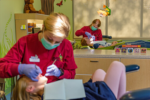 A setting picture of 2 dentists in red scrubs cleaning 2 children's teeth